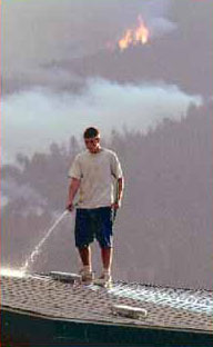 A resident in the Bitterroot Valley of Montana soaks his home's roof during the wildfires of 2000