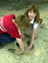 Children comparing their hand sizes to that of a dinosaur's prehistoric footprint.
